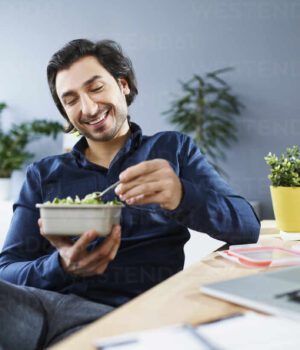 Katowice, Silesia, Poland. Happy man eating lunch while working in small office